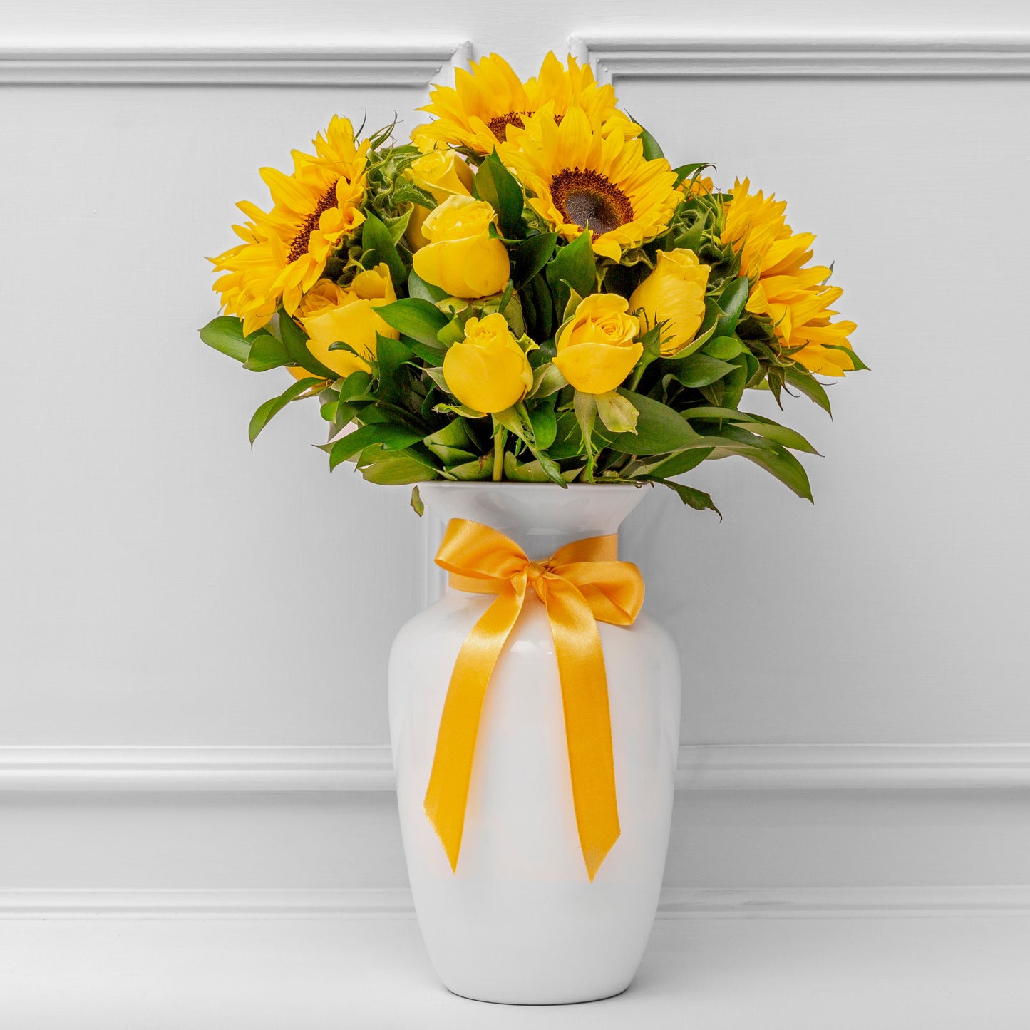 Elegant Women's Day flower arrangement with fresh sunflowers and yellow roses in a white ceramic vase with a yellow ribbon. Perfect gift for Women's Day in Medellín with same-day delivery.