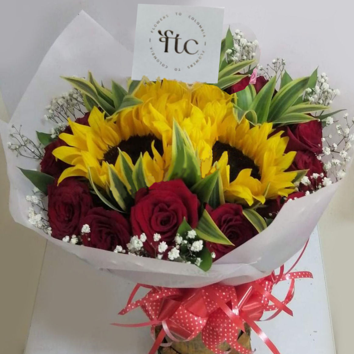  bouquet of vibrant sunflowers, red roses, baby’s breath, and greenery, wrapped with a stylish ribbon. Perfect for delivery in Cartago, Valle.