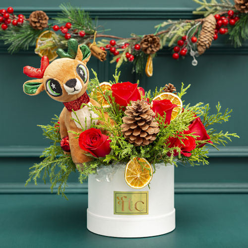 Christmas arrangement with red roses, green foliage, dried orange slices, pinecones, and reindeer decoration for delivery in Medellín, Colombia.