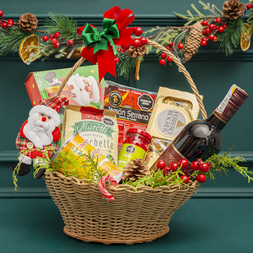 Elegant Christmas hamper in a wicker basket with Estoril wine, cookies, Serrano ham, bruschette chips, preserved peaches, cherries, Ferrero chocolates, pine tree decorations, pinecones, bows, and candy canes.