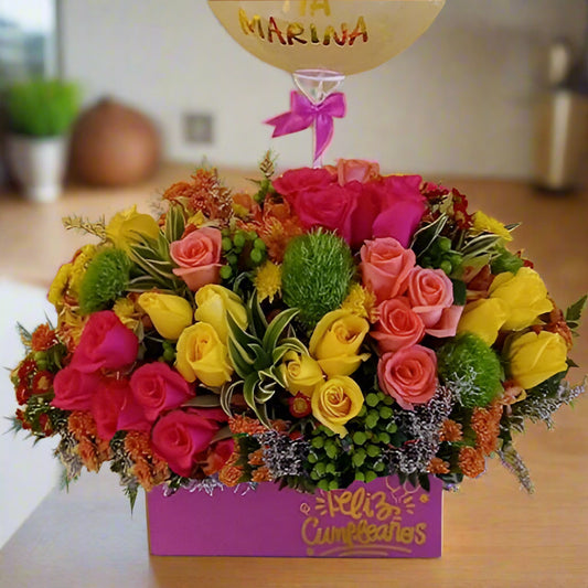 Vibrant floral arrangement with multicolor roses, lush greenery, and a festive birthday balloon in a pink gift box. Perfect for birthday celebrations with delivery in Cali and Bogotá.